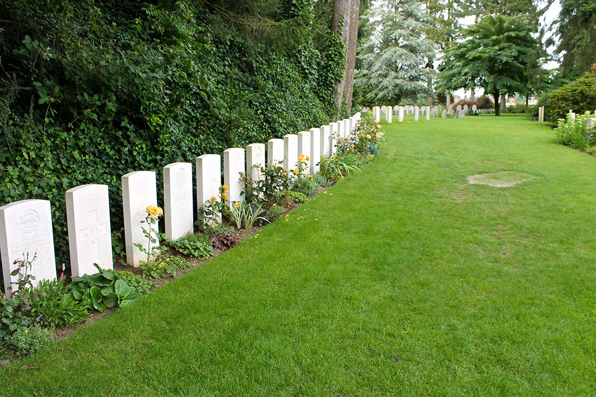 A row of white stone gravestones with flowers on a neat green lawn